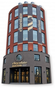 Округлый краснокирпичный входной корпус Chocolate Nation в Антверпене с серыми вывесками и стеклянным входом